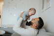 © Johnér - Happy father carrying baby boy while sitting on sofa in living room