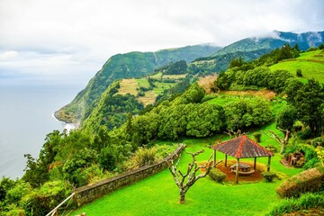 Wall Mural - Aerial view of a lush grassy field situated along the coast, surrounded by majestic mountains