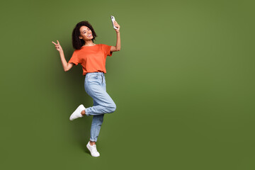 Sticker - Full length photo of funky friendly woman wear orange t-shirt showing v-sign taking selfie gadget empty space isolated green color background