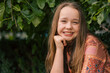 © Austockphoto - Portrait of pre-teen girl sitting on brick wall with natural green leafy background