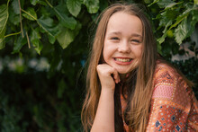 Portrait Of Pre-teen Girl Sitting On Brick Wall With Natural Green Leafy Background