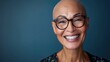 A bald smiling woman with glasses and a blue background.