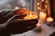 © Yuliia - Close up unrecognizable calm relaxed Caucasian woman female lady girl hands holding burning lighted aroma scented candle night indoors home living room window. Cozy evening house comfort aromatherapy