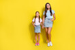 Full length photo of pretty good mood small siblings dressed t-shirts holding hands arms empty space isolated yellow color background