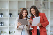 © amnaj - Two professional women collaborating on a project using a tablet in a contemporary office.