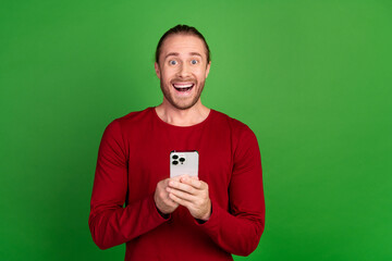 Poster - Portrait of satisfied impressed guy with long hair wear red shirt hold smartphone asstonished staring isolated on green color background