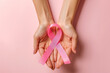 Woman hands holding a pink ribbon on a pink background 