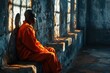 Side view of a bald African young man in an orange prisoner uniform sitting on a stone bench in a prison corridor