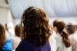 © Aleksey - Curly-haired Woman in Purple Sweater at Conference Listening to Speaker