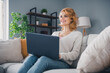 © deagreez - Portrait of cheerful lovely lady sitting comfy sofa use laptop brainstorming free time apartment inside