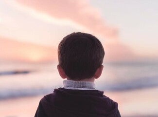 Wall Mural - Child looking to the sea. Unrecognizable boy staring to the ocean on the beach at beautiful pink sunset. Travel on summer.