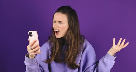 Wall Mural - Mad and shock young brunette beautiful woman using mobile phone isolated on purple background. Yelling unhappy woman hold mobile phone. Disappointed sad upset lady horrified impressed news. WTF. Oh no