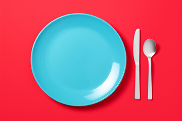 Blue plate with knife and spoon on red background. Mock-up design, minimalistic table setting, modern dining