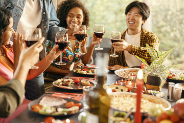 Wall Mural - Group of happy young friends is drinking wine while having holiday dinner home party together