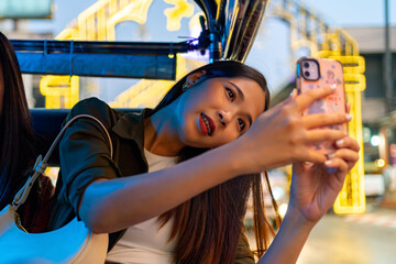 Asian woman enjoy outdoor lifestyle travel in Thailand on summer holiday vacation. Happy girl using mobile phone taking picture during travel Chiang Mai city by three wheeled vehicles Tuk Tuk car.