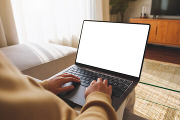 Mockup image of a woman working and typing on laptop computer with blank screen while sitting on sofa at home