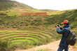 © jobi_pro - Traveler taking photos of the remains of Moray, an Incan agricultural terraces in Sacred Valley of the Incas, Cusco Region, Peru, South America