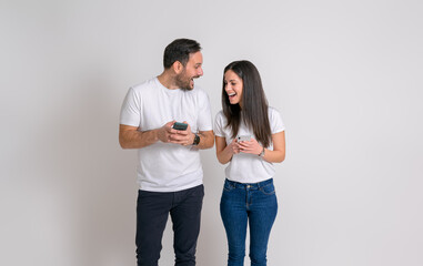 Wall Mural - Young boyfriend and girlfriend with smart phones texting and laughing cheerfully on white background