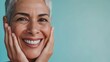 © Z A C - Smiling woman with short gray hair holding her cheeks against a light blue background.