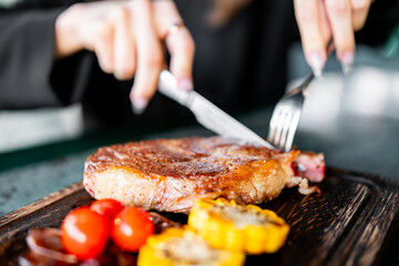 Wall Mural - woman hands with fork and knife eating beef steak in cafe