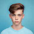 Portrait of a serious teenage boy with brown hair on a blue background. Closeup face of an unhappy Caucasian young adult looking at the camera. Front view of an unsmiling white kid in a blue shirt.