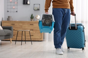 Sticker - Travel with pet. Man holding carrier with cute cat and suitcase at home, closeup. Space for text