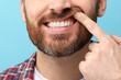 © New Africa - Man showing his healthy teeth and gums on light blue background, closeup