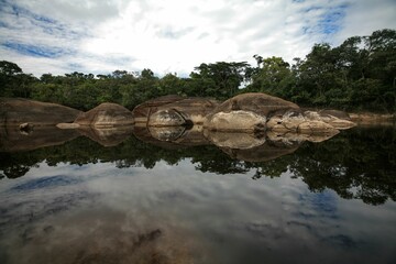 Poster - rocks in the water next to the forest and sky with clouds