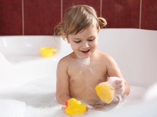 Poster - Smiling girl bathing with toy ducks in tub