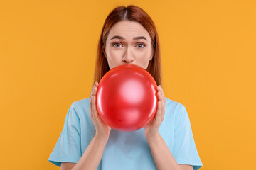 Canvas Print - Woman inflating red balloon on orange background