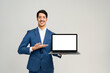 Man in a smart blue suit stands against a clean background, holding a laptop with a blank screen towards the camera, the perfect template for graphic designers to superimpose an application or website