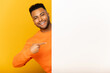 © Vadim Pastuh - Look here. Smiling indian man peeking out from behind white empty paper poster, presenting novelty, arab guy paying attention at blank billboard banner isolated on yellow, copyspace, advertising