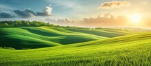The sun is descending, casting its warm golden sunlight over a lush green field with rolling hills in the background.
