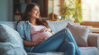 Mulher gravida feliz com a mão na barriga sentada no sofá de casa