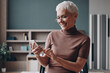 © gstockstudio - Senior businesswoman using smart phone and smiling while leaning at the office desk
