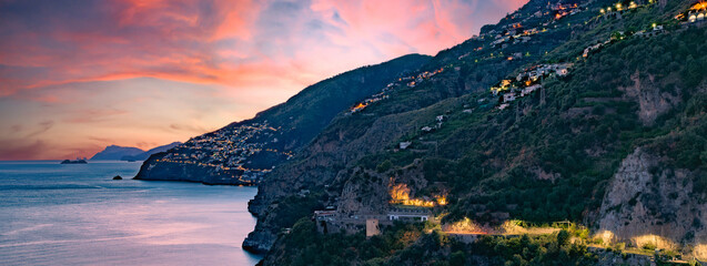 Wall Mural - Amalfi Coast, Italy. View over Praiano on the Amalfi Coast at sunset. Street and house lights at dusk. In the distance the island of Capri on the horizon. Sea landscape. Banner header image.