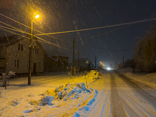 Wall Mural - Snow falls in the light of a street lamp near the road at night