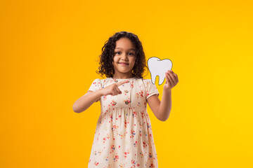 Child girl holding papercraft tooth and pointing finger at it. Dental health concept