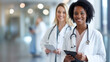 © MP Studio - smiling female healthcare professional in the foreground holding a clipboard with a stethoscope around her neck
