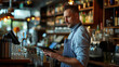 © MP Studio - focused bearded man in a blue striped apron using a tablet in a bar setting