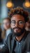 © TheGoldTiger - A man with glasses and curly hair, sporting a beard, looks pensive in a softly lit room, generative ai