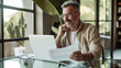 © MP Studio - A joyful person reviewing documents at a table with a laptop, showing a scene of productivity and contentment.