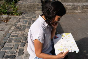 Latin woman resting and consulting a map sitting in a park in Dublin to recognize the next destination to visit in the city