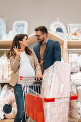 Wall Mural - Attractive middle age couple enjoying in buying clothes and appliances for their new baby. Heterosexual couple in baby shop or store. Expecting baby concept.