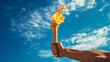 A man hand holds a torch with the Olympic flame against a blue sky background