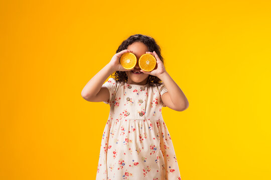 Smiling kid girl holding half of oranges near the eyes. Healthy food, vitamins and children nutrition concept