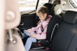 © Aleksandr - Cute little girl use tablet in car seat on the way to the kindergarten