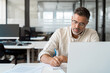 © Stock 4 You - Focused middle-age Hispanic man using laptop computer for business studying, watch online virtual webinar training meeting, video call, make notes. Mature Latin businessman work in office, copy space.