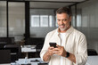 © Stock 4 You - Smiling mature Latin or Indian businessman holding smartphone in office. Middle aged manager using cell phone mobile app. Digital technology application and solutions for business success development.