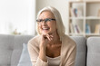 © fizkes - Happy blonde old senior woman in elegant glasses looking away home portrait. Cheerful positive elder female model leaning chin on hand, thinking on retirement with toothy smile
